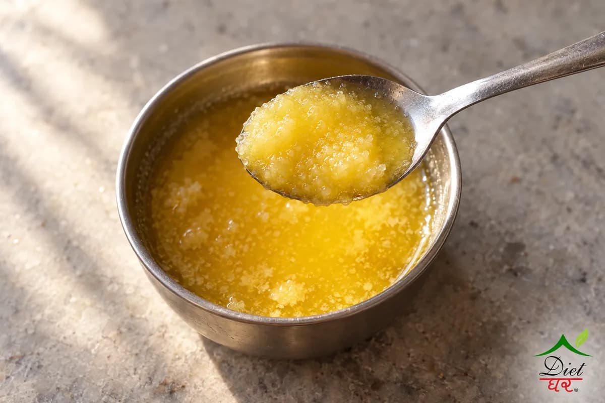 A teaspoon of golden desi ghee held above a steel bowl of ghee