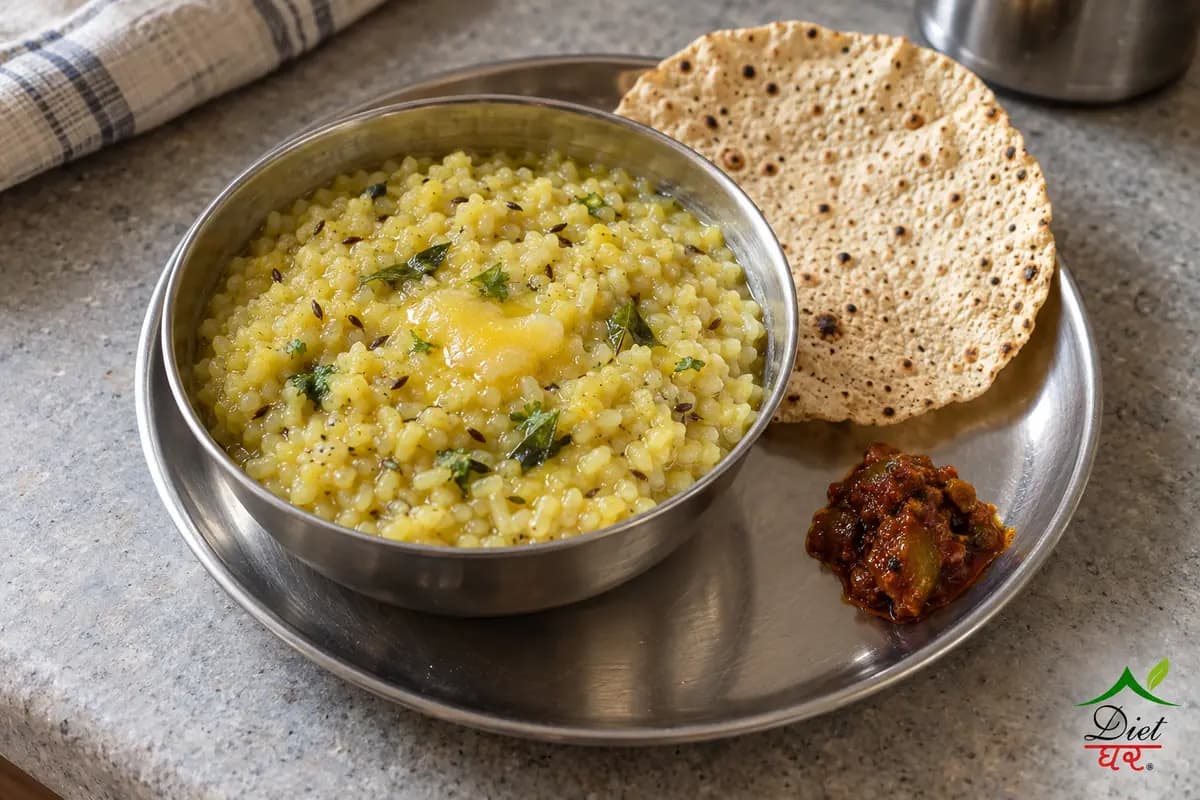 Moong dal khichdi in a steel bowl with ghee on top, with papad and pickle