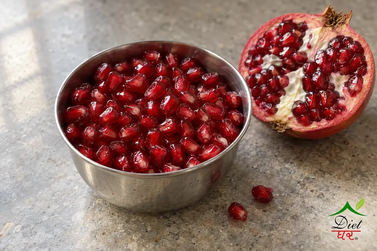 Pomegranate seeds in a steel katori beside half a pomegranate